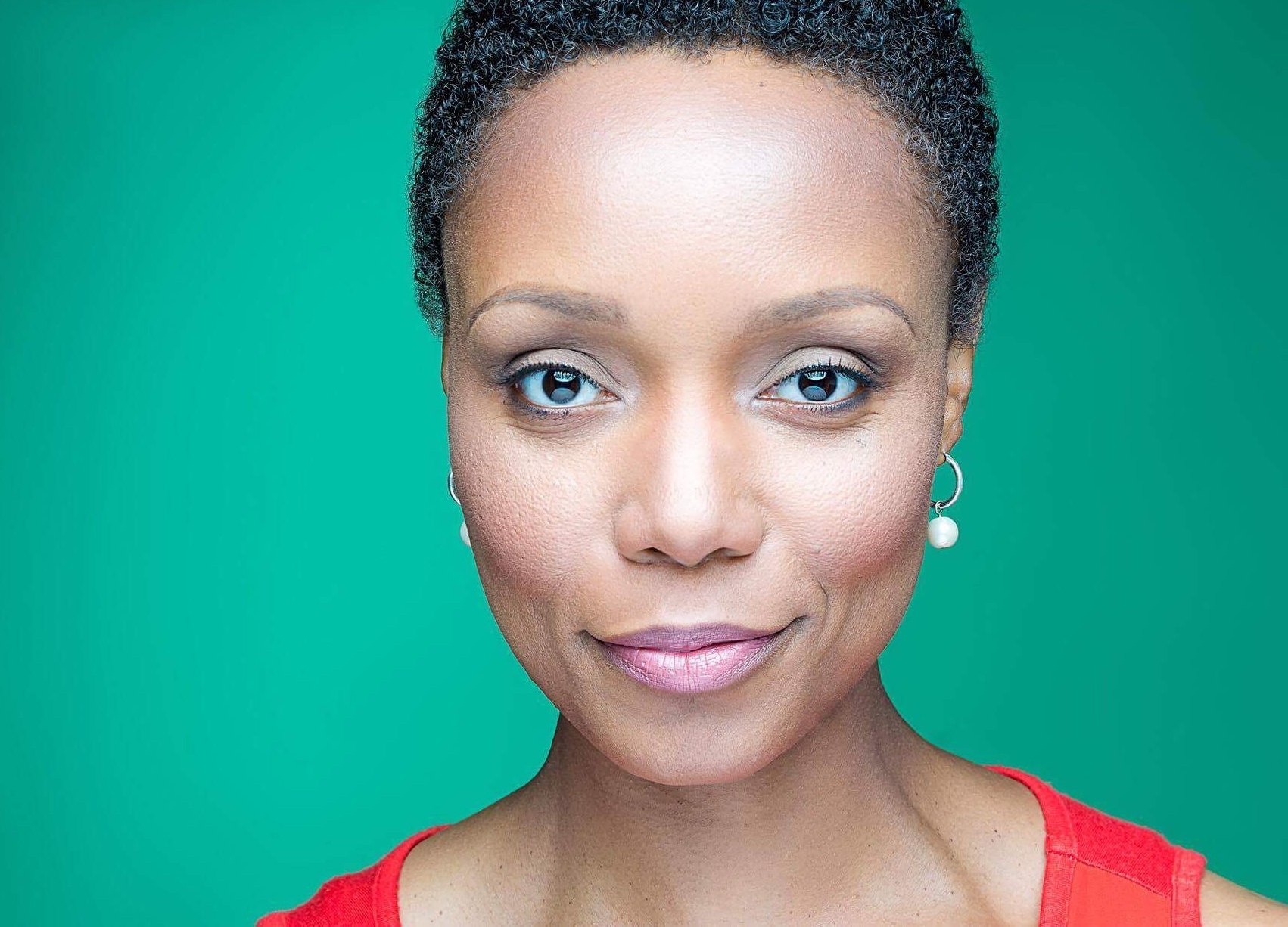 A headshot of Malkia Stampley, a Black woman with short hair and a red shirt, in front of a green background.