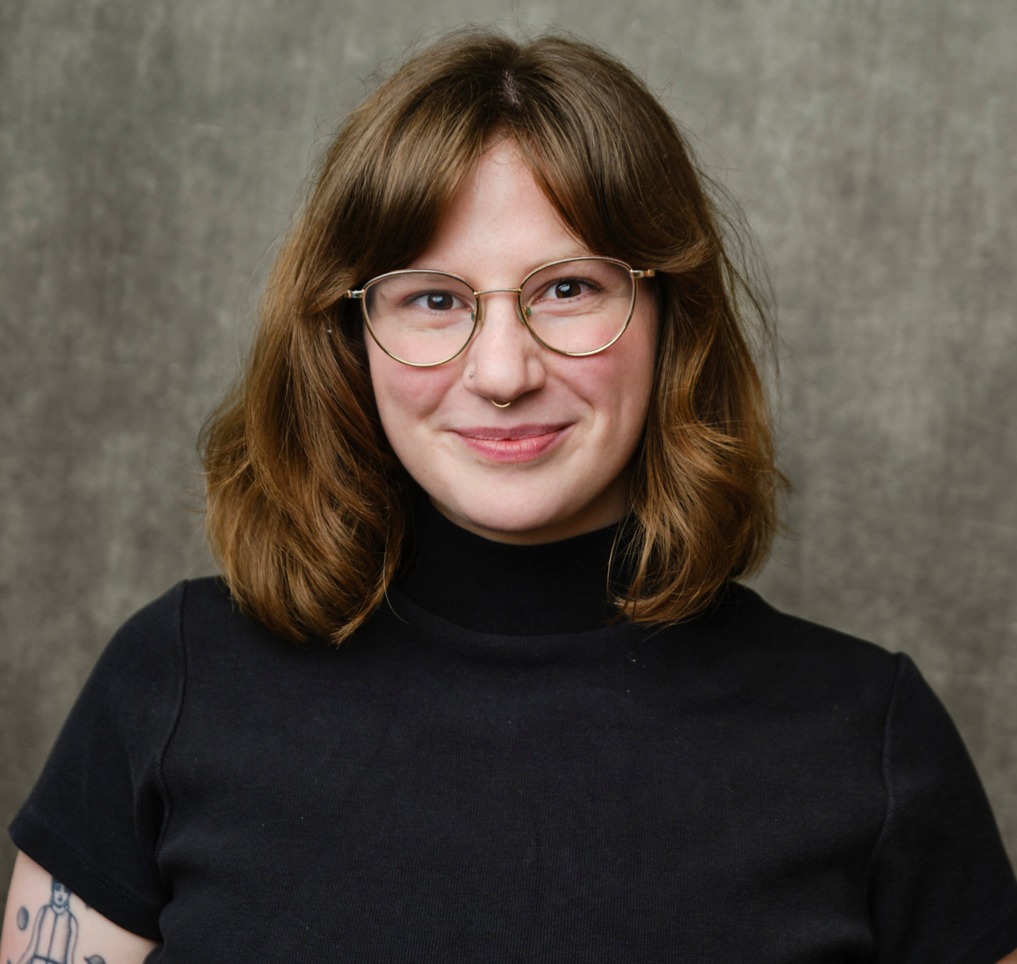 An image of Molly Sharfstein, a white person with brown shoulder-length hair and glasses, in front of a grey background